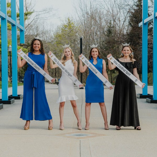 Four women holding sashes and wearing crowns stand under the Transformational Link