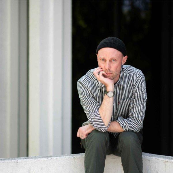 A person sits with their chin resting in their hand. Their other arm is resting atop their legs.