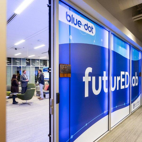 A sign with different shades of blue is seen in windows to a glassed-in office area. The signs contain the words "blue dot" and "futureEDlab."