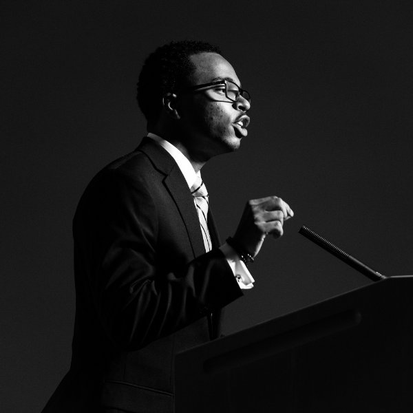 Julian Sanders gives remarks at a podium, in a black and white photo