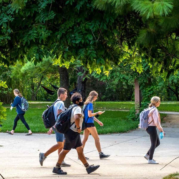 students walking outside on Allendale Campus sidewalk with green trees in the background