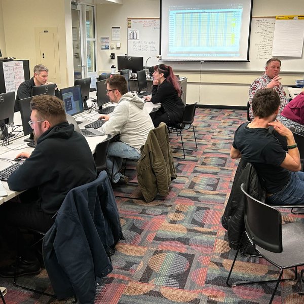 people in a computer lab working on their desktops, chatting with each other