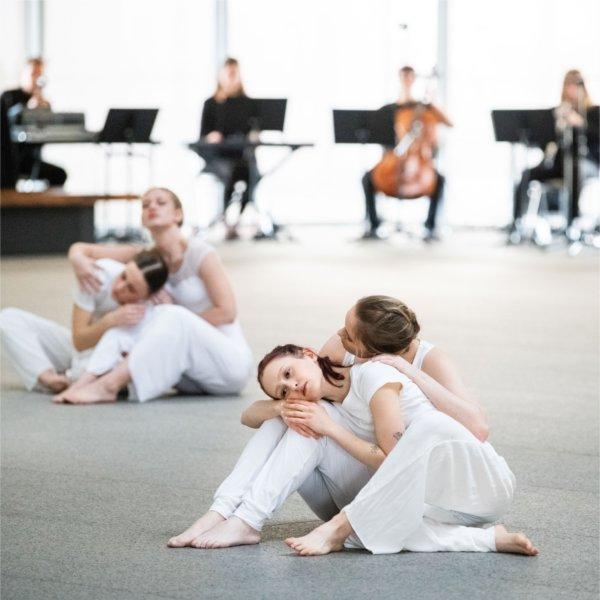 Dancers wearing white perform in front of musicians in the background.