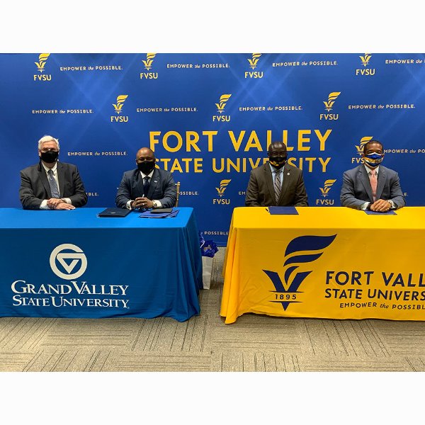 four people in masks seated at tables in front of sign at Fort Valley State University.
