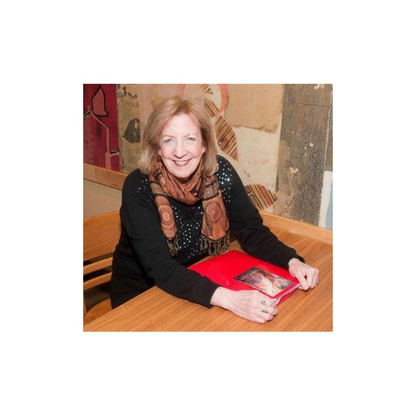 A person smiles while seated at a wooden table. A red folder sits between each hand and arm.