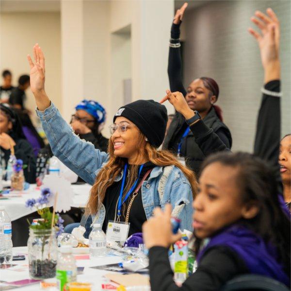 Students raise their hands to be called on while sitting at a table.