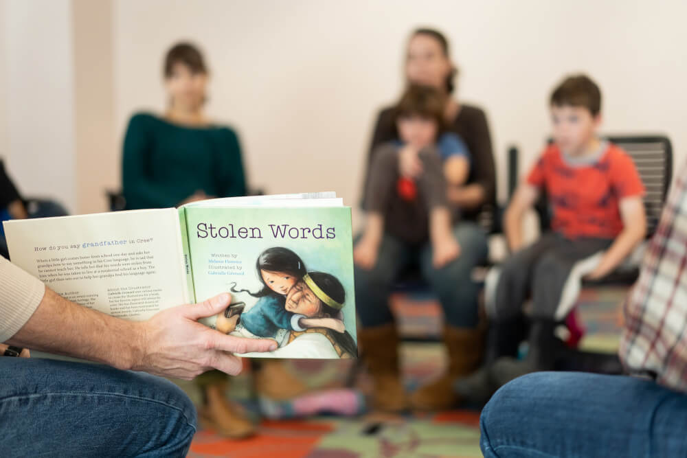 A group of children listen to some one reading the book, "Stolen Words."