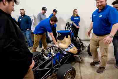 Louie the Laker sits in a car that resembles a go-kart created by engineering students
