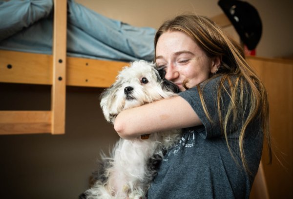  A college student hugs her dog while inside a dorm room. 