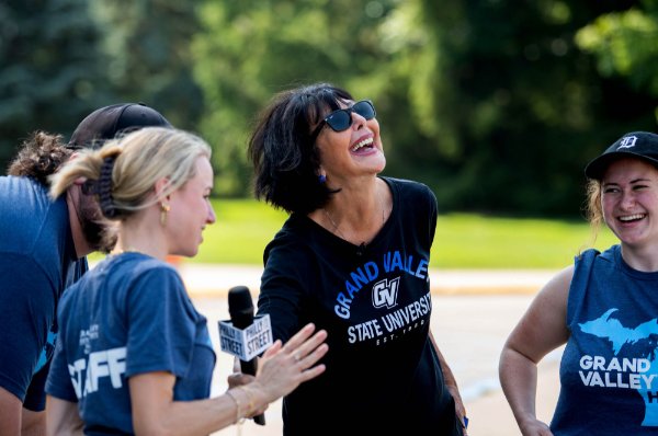  A college president wearing sunglasses laughs with college students. 