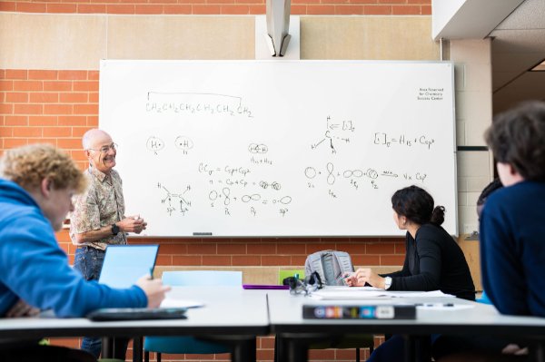 A college professor talks through problems on a whiteboard during a study group.  