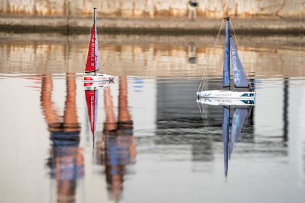  Students are reflected into water while they sail small remote control sailboats on a pond. 