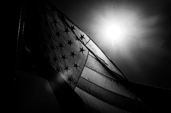 A black and white image of the U.S. flag waving in the wind. 