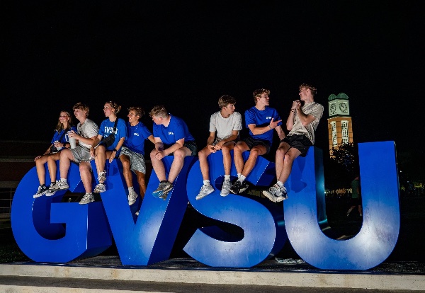 Students sit atop a GVSU sign on the Allendale campus during a campus kickoff event.