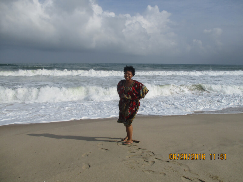 Elayne Vaugn stands on a beach next to the ocean.
