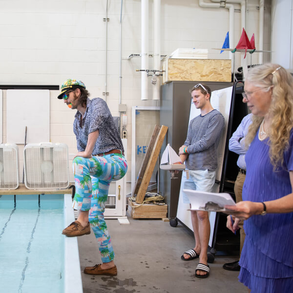 An engineering student, dressed for the regatta in a captain's hat and nautical-themed pants, watches his boat cross the test tank.