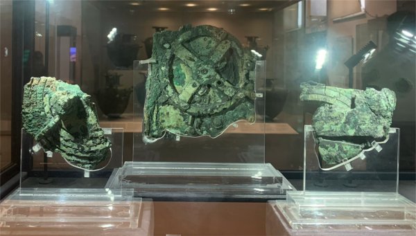 An artifact in three pieces, with a green coloring, is seen through a glass box.