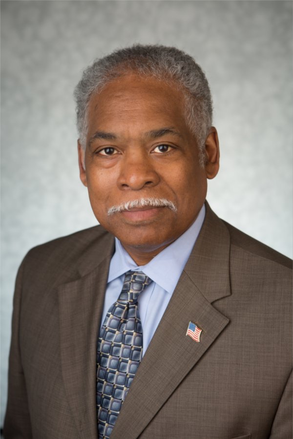 headshot of James Moyer, in brown jacket, light shirt and tie