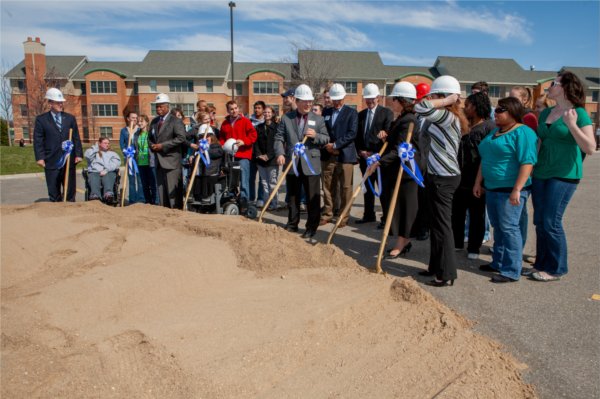group of people, front row wearing hard hats, with shovels in front of a mound of dirt