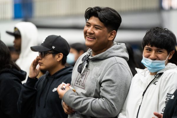 four students standing, center student laughing and person on right is wearing a mask