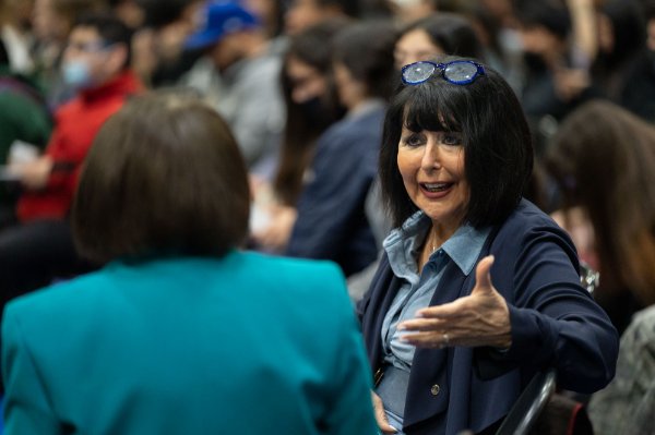 President Mantella seated, speaks to Lupe Ramos, who has back to camera and is wearing a blue-green jacket.