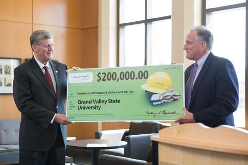  President Thomas J. Haas, left, and Trustee John Russell hold a check, signifying a donation from Consumers Energy Foundation to enhance services at the Oliver Wilson Freshman Academy.