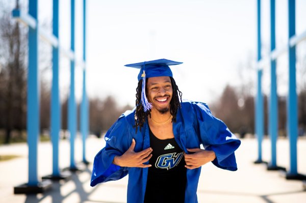 A person wearing a cap and gown smiles while showing a top with the words "adidas" and the initials "GV" on a shirt.