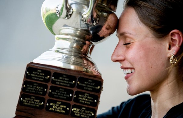  A student holds a trophy and touches it to her forehead with a smile on her face and eyes closed. 
