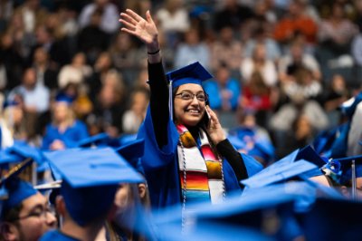 A graduating student stands and waves at her family at a commencement ceremony. 
