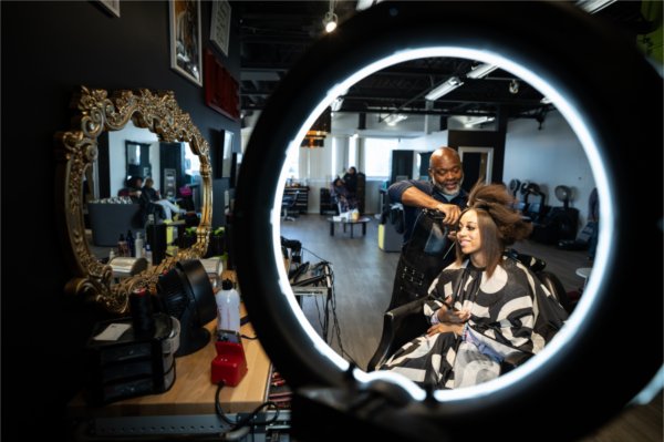 Salon owner Jerry Wright works on a client's hair, they are projected in a mirror