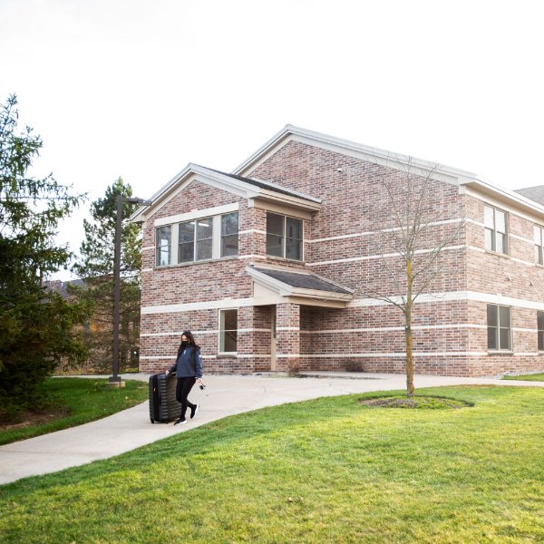 A student pulling a suitcase outside a living center on the Allendale Campus.