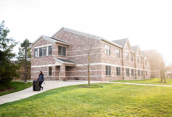 A student pulling a suitcase outside a living center on the Allendale Campus.