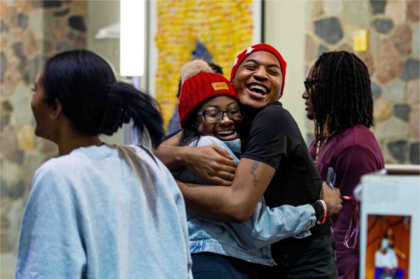  Two people wearing red winter hats embrace with big smiles on their faces. 