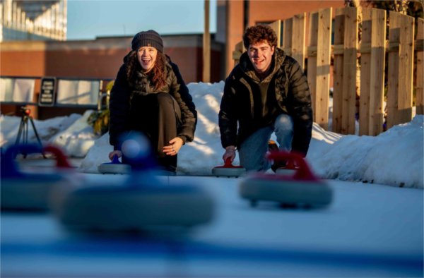  Two college students smile as they crouch down to play a game of curling. 