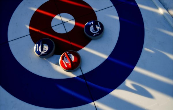  The sunlight casts shadows on curling stones of red and blue. 