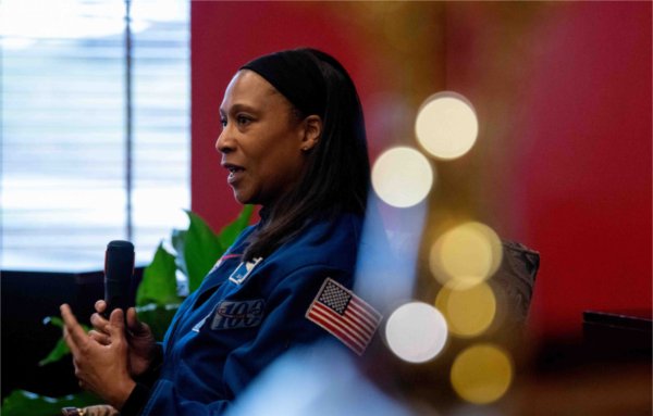  An astronaut speaks with a microphone in their hands with sparkling lights in the foreground.