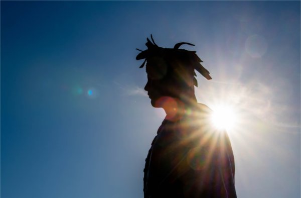  A sun bursts shows behind a bronze statue of a chief. 