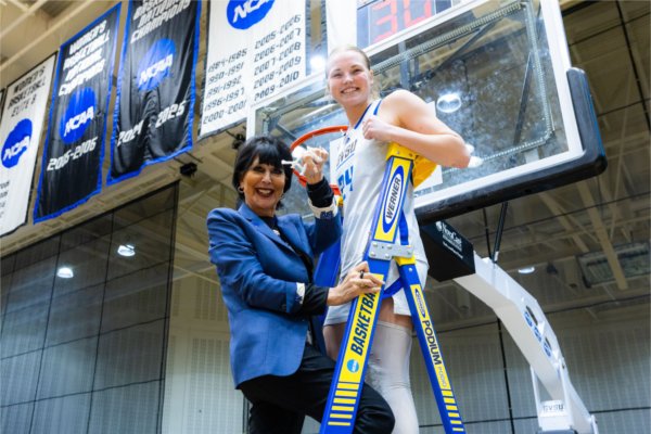 A university president climbs a later with a women's basketball player to cut the net. 