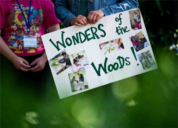 A teacher holds a sign showing off their student project "Wonders of the Woods!" during the Groundswell Stewardship Initiative student project showcase on the Pew Grand Rapids Campus May 15.