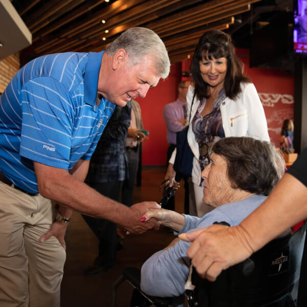 man meeting woman in wheelchair: President Emeritus Thomas J. Haas meets President Philomena Mantella's mother, Lucille, at the Grand Rapids Downtown Market.