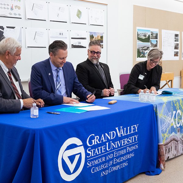 four people seated at table signing documents; half the table has GVSU tablecloth, half of it is a Kendall College of Art and Design tablecloth