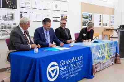four people seated at table signing documents; half the table has GVSU tablecloth, half of it is a Kendall College of Art and Design tablecloth