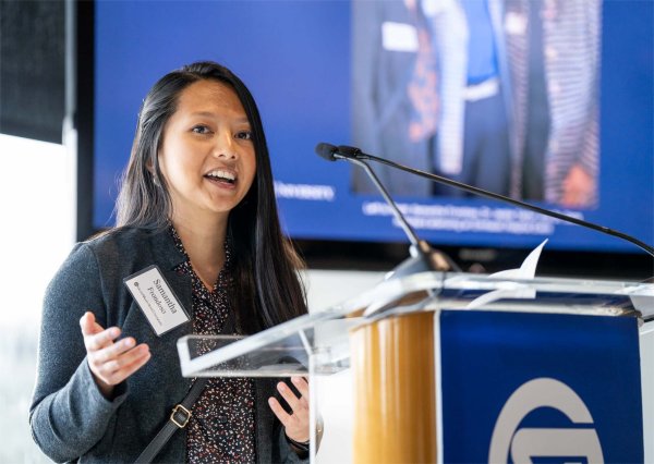 A person smiles and gestures while speaking from a podium.