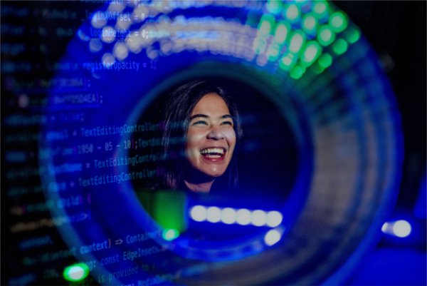 A college student smiles as seen through a round blue and green shape with computer coding double exposed. 