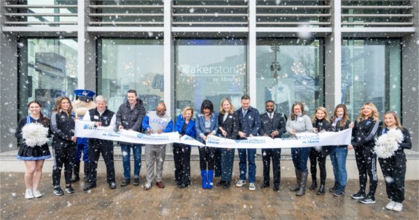 Large snowflakes fall during a ribbon cutting ceremony outside a glass storefront. 