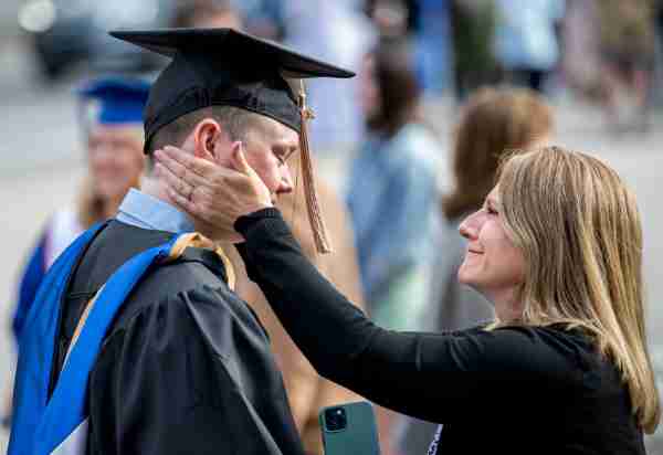A grad greets his mother who places a hand on his cheek after the ceremony.