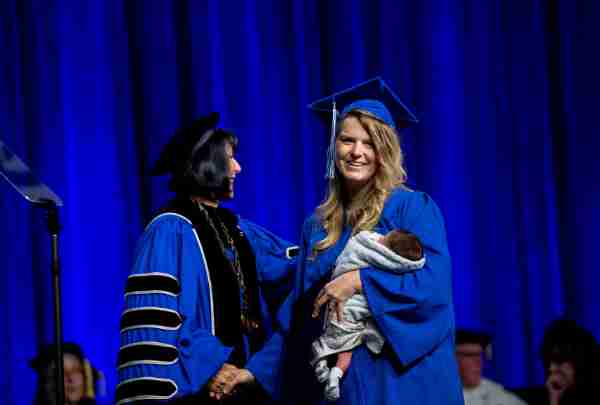 A grad shakes President Mantella's hand while carrying a baby in her arms.