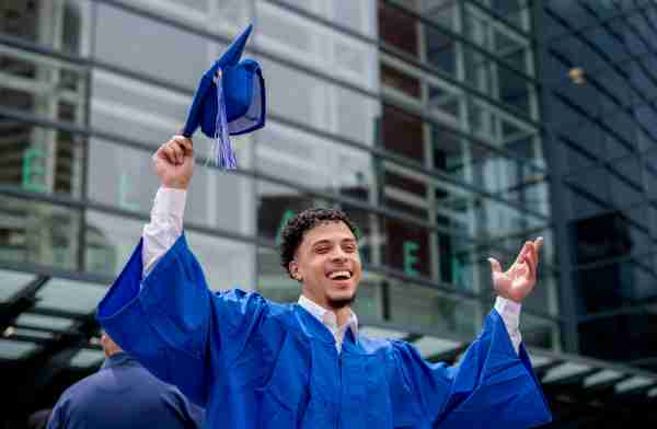 A grad holds his cap above his head in triumph in front of Van Andel Arena.