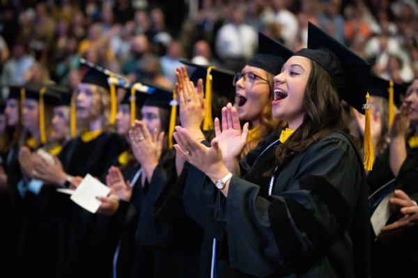 Grads in Masters robes clap and cheer during the ceremony.