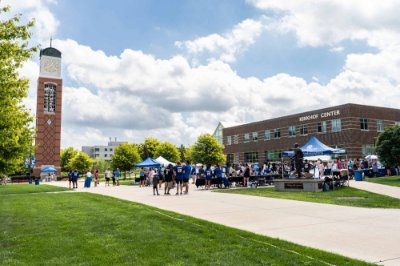large crowd at outdoor tents outside the Kirkhof Center with carillon tower in view
